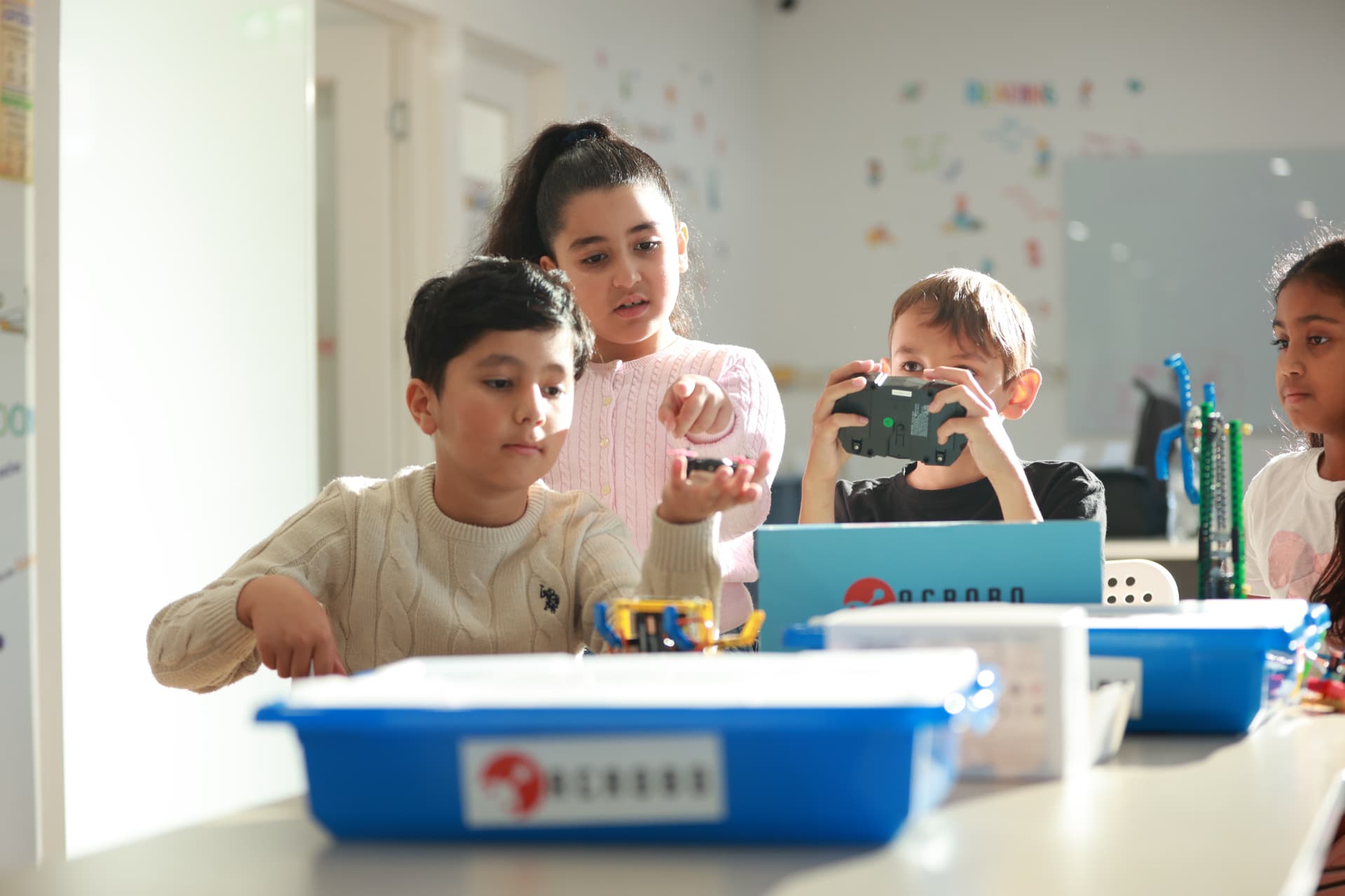 Four ACROBO students at a bench with robotics kits, testing a build with a controller