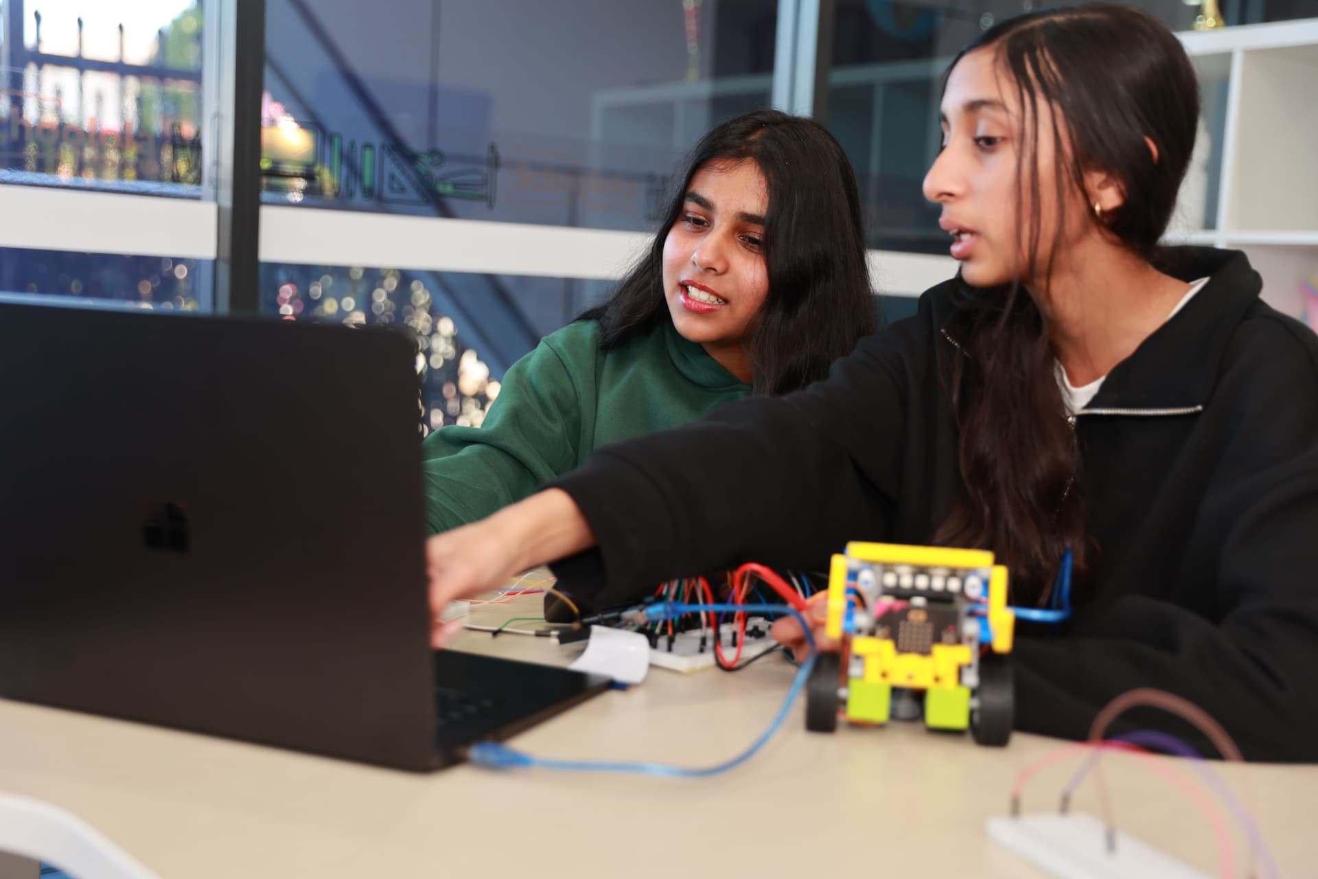 Two ACROBO students testing a wheeled robot build with a laptop in class